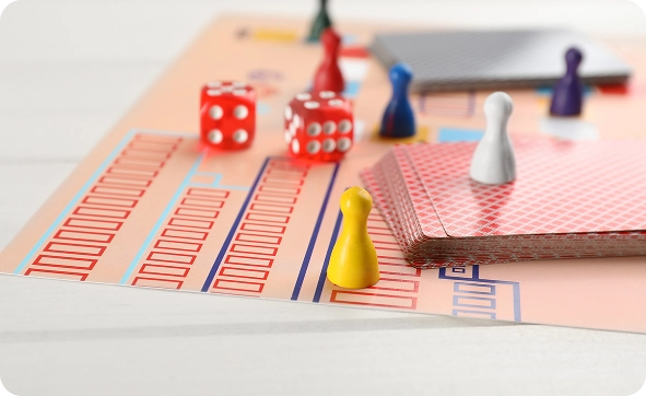 Jogo de tabuleiro colorido com cartas, dados e peças de madeira dispostas num tabuleiro, perfeito para noites de jogos em família e jogos de estratégia de mesa.