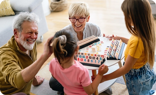 Uma família multigeracional a desfrutar de um jogo de tabuleiro em casa, criando momentos memoráveis com jogos de mesa clássicos para todas as idades.